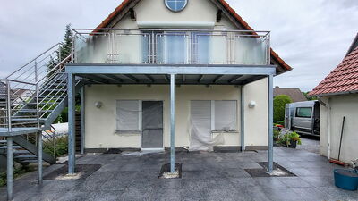 Blick auf einen verzinkten Anbaubalkon mit Edelstahlgeländer und Glasfüllung, Links daneben eine verzinkte Stahltreppe